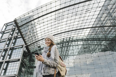 Glückliche junge Frau mit Smartphone am Hauptbahnhof, Berlin, Deutschland - AHSF01484