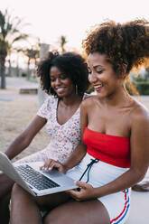 Junge Frauen benutzen einen Laptop in einem Park - MPPF00315