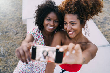 Young women smiling and making a selfie with their smart phone in a park, focus on background - MPPF00316
