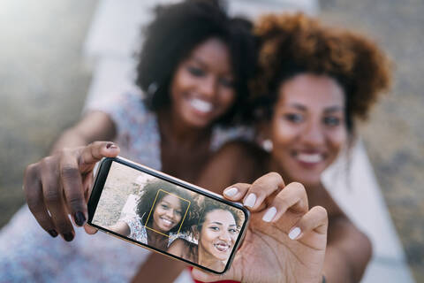 Junge Frauen lächeln und machen ein Selfie mit ihrem Smartphone in einem Park, lizenzfreies Stockfoto