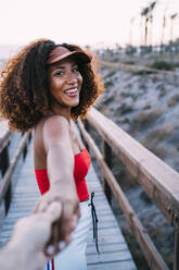 Lächelnde junge Frau mit brauner Mütze führt ihre beste Freundin an den Strand - MPPF00320