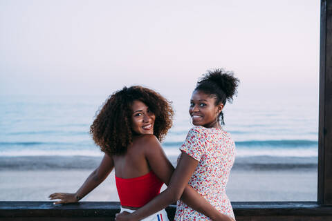 Best friends standing arm in arm on pier, turning around and looking at camera in the evening stock photo