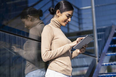 Young woman using tablet on exterior stairs - JSMF01368