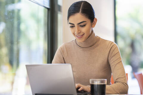 Lächelnde junge Frau mit Laptop in einem Cafe, lizenzfreies Stockfoto