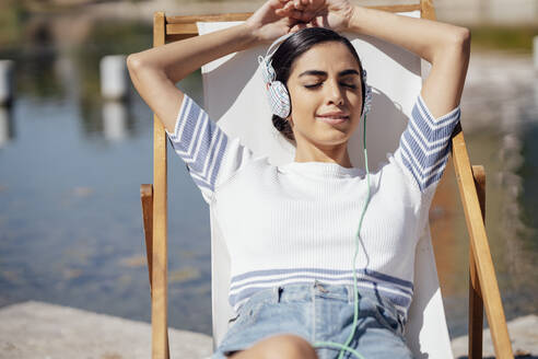 Junge Frau mit Kopfhörern, die sich in einem Liegestuhl entspannt - JSMF01386