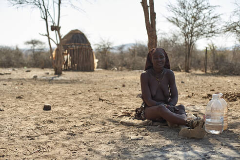 Himba-Frau, die in ihrem Dorf auf sandigem Boden sitzt, Opuwo, Namibia - VEGF00933