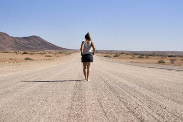 Frau geht in der Mitte einer unbefestigten Straße, Damaraland, Namibia - VEGF00937