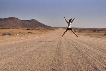 Woman jumping in the middle of a dirt road, Damaraland, Namibia - VEGF00938