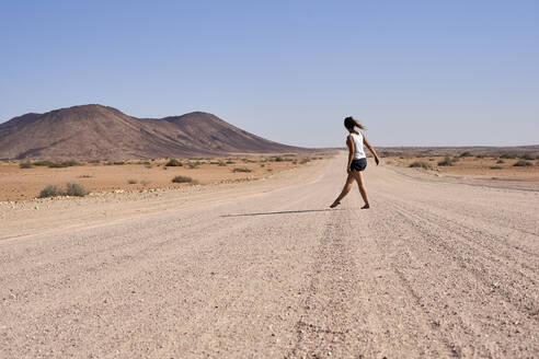 Frau geht in der Mitte einer unbefestigten Straße, Damaraland, Namibia - VEGF00939
