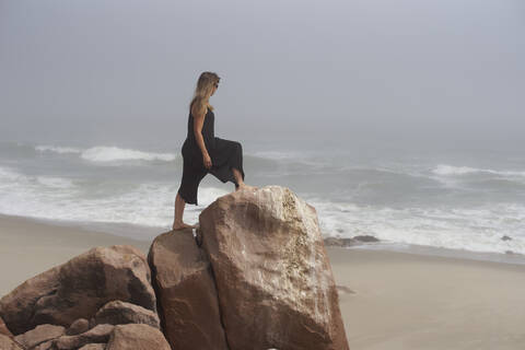 Frau steht auf einem Felsen und schaut auf den Ozean, Cape Cross, Namibia, lizenzfreies Stockfoto