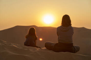 Mutter und Tochter sitzen bei Sonnenuntergang in den Wüstendünen, Düne 7, Walvis Bay, Namibia - VEGF00954