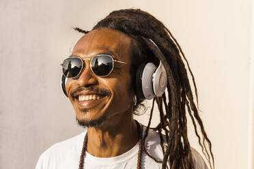 Porträt eines lächelnden reifen Mannes mit Dreadlocks und Kopfhörern, der Musik hört und zur Seite schaut - TCF06210
