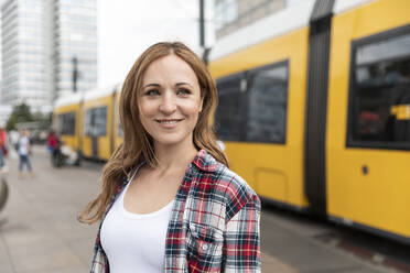 Smiling woman in the city with a tram in the background, Berlin, Germany - WPEF02294