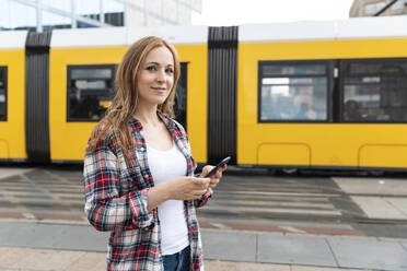 Porträt einer lächelnden Frau in der Stadt mit einer Straßenbahn im Hintergrund, Berlin, Deutschland - WPEF02295