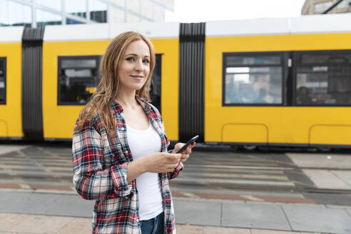 Portrait of a smiling woman in the city with a tram in the background, Berlin, Germany - WPEF02295