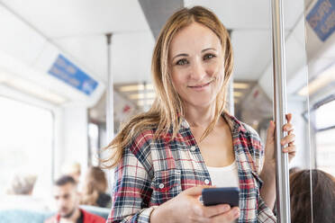 Portrait of smiling woman with smartphone on the subway, Berlin, Germany - WPEF02308
