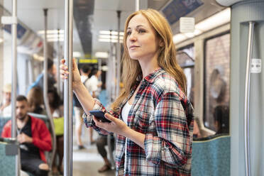 Smiling woman with smartphone on the subway, Berlin, Germany - WPEF02309