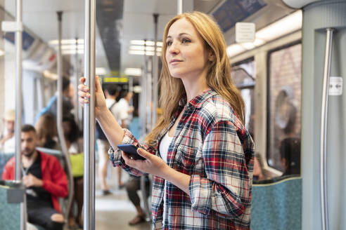 Lächelnde Frau mit Smartphone in der U-Bahn, Berlin, Deutschland - WPEF02309