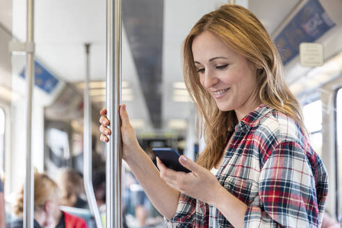 Lächelnde Frau schaut in der U-Bahn auf ihr Smartphone, Berlin, Deutschland - WPEF02310