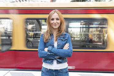 Porträt einer lächelnden Frau mit verschwommenem Zug im Hintergrund am Bahnhof, Berlin, Deutschland - WPEF02316