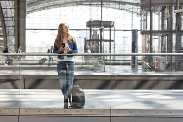 Frau mit Smartphone auf dem Bahnhof, die sich umschaut, Berlin, Deutschland - WPEF02318