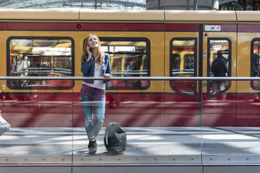 Lächelnde Frau am Telefon auf dem Bahnhof, Berlin, Deutschland - WPEF02319