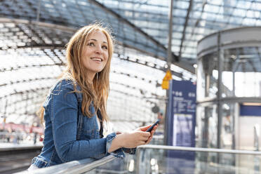 Smiling woman with smartphone at the train station, Berlin, Germany - WPEF02320