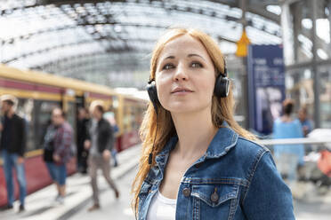 Porträt einer Frau, die mit Kopfhörern auf dem Bahnhof Musik hört, Berlin, Deutschland - WPEF02323