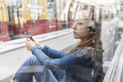 Frau mit Smartphone und Kopfhörern wartet am Bahnhof, Berlin, Deutschland, lizenzfreies Stockfoto