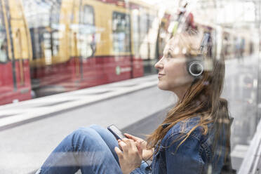 Woman with smartphone and headphones waiting at the station, Berlin, Germany - WPEF02330