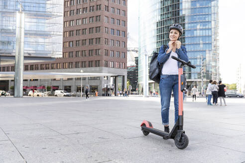 Frau mit E-Scooter in der Stadt setzt Helm auf, Berlin, Deutschland - WPEF02347