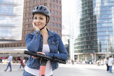 Portrait of smiling woman with e-scooter in the city, Berlin, Germany - WPEF02348