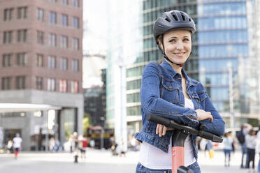 Portrait of smiling woman with e-scooter in the city, Berlin, Germany - WPEF02350