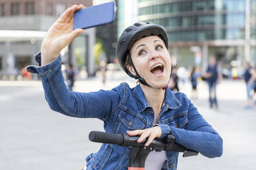 Glückliche Frau mit E-Scooter, die ein Selfie in der Stadt macht, Berlin, Deutschland - WPEF02351