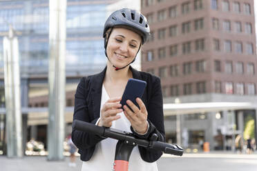 Frau mit E-Scooter und Smartphone in der Stadt, Berlin, Deutschland - WPEF02355