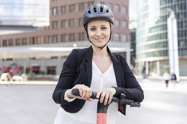 Portrait of smiling woman with e-scooter in the city, Berlin, Germany - WPEF02359