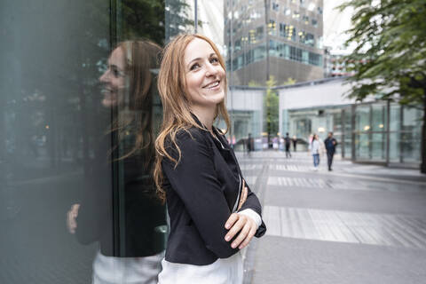 Lächelnde Geschäftsfrau lehnt an einem Gebäude in der Stadt, lizenzfreies Stockfoto