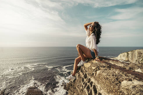 Junge Frau sitzt auf einem Aussichtspunkt mit der Hand im Haar, Getxo, Spanien - MTBF00236