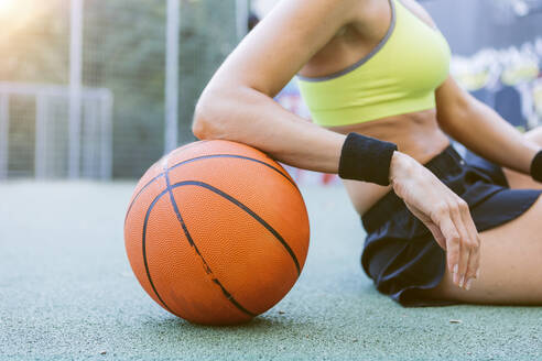 Junge Frau sitzt und ruht sich auf einem Basketball aus - MADF01411