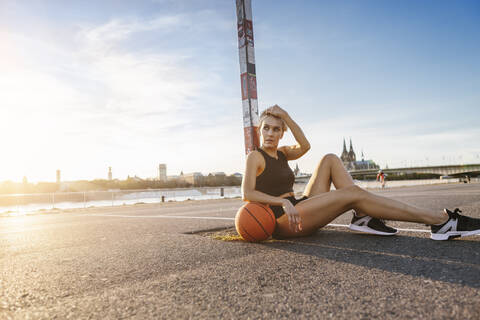 Blonde Frau sitzt mit Basketball auf einem Spielfeld in Köln, Deutschland, lizenzfreies Stockfoto