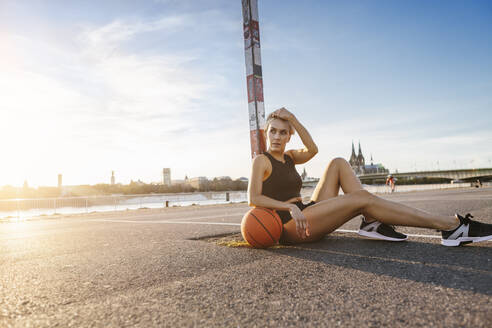 Blonde Frau sitzt mit Basketball auf einem Spielfeld in Köln, Deutschland - MADF01430