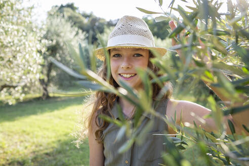 Smiling girl with straw hat standing in an olive grove, Tuscany, Italy - OJF00360