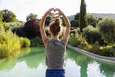 Rear view of a girl standing at swimming pool, forming a heart with her hands - OJF00362