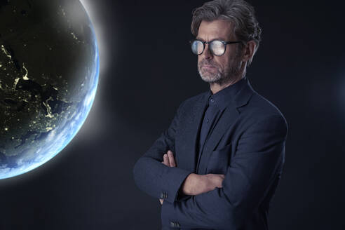 Portrait of mature businessman against dark background watching floating planet earth - PHDF00006