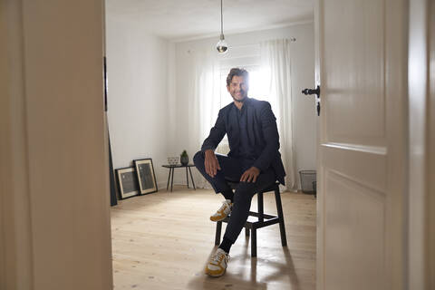 Porträt eines lächelnden reifen Mannes, der zu Hause auf einem Hocker sitzt, lizenzfreies Stockfoto