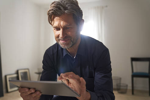 Porträt eines lächelnden reifen Mannes, der zu Hause ein digitales Tablet benutzt - PHDF00012