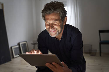 Porträt eines lächelnden reifen Mannes, der sich zu Hause mit einem digitalen Tablet amüsiert - PHDF00013