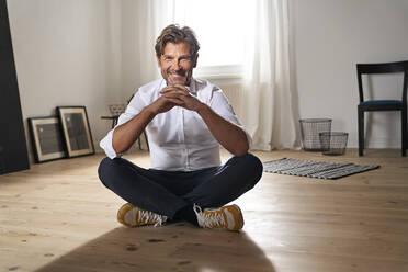 Porträt eines lächelnden reifen Mannes, der zu Hause auf dem Boden sitzt - PHDF00019