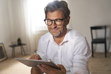 Portrait of smiling mature man wearing glasses using digital tablet at home - PHDF00022