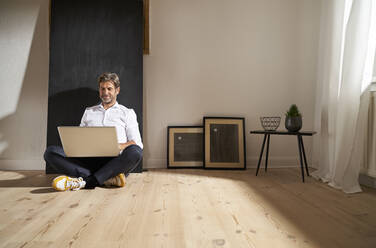 Entspannter reifer Mann, der zu Hause auf dem Boden sitzt und einen Laptop benutzt - PHDF00025